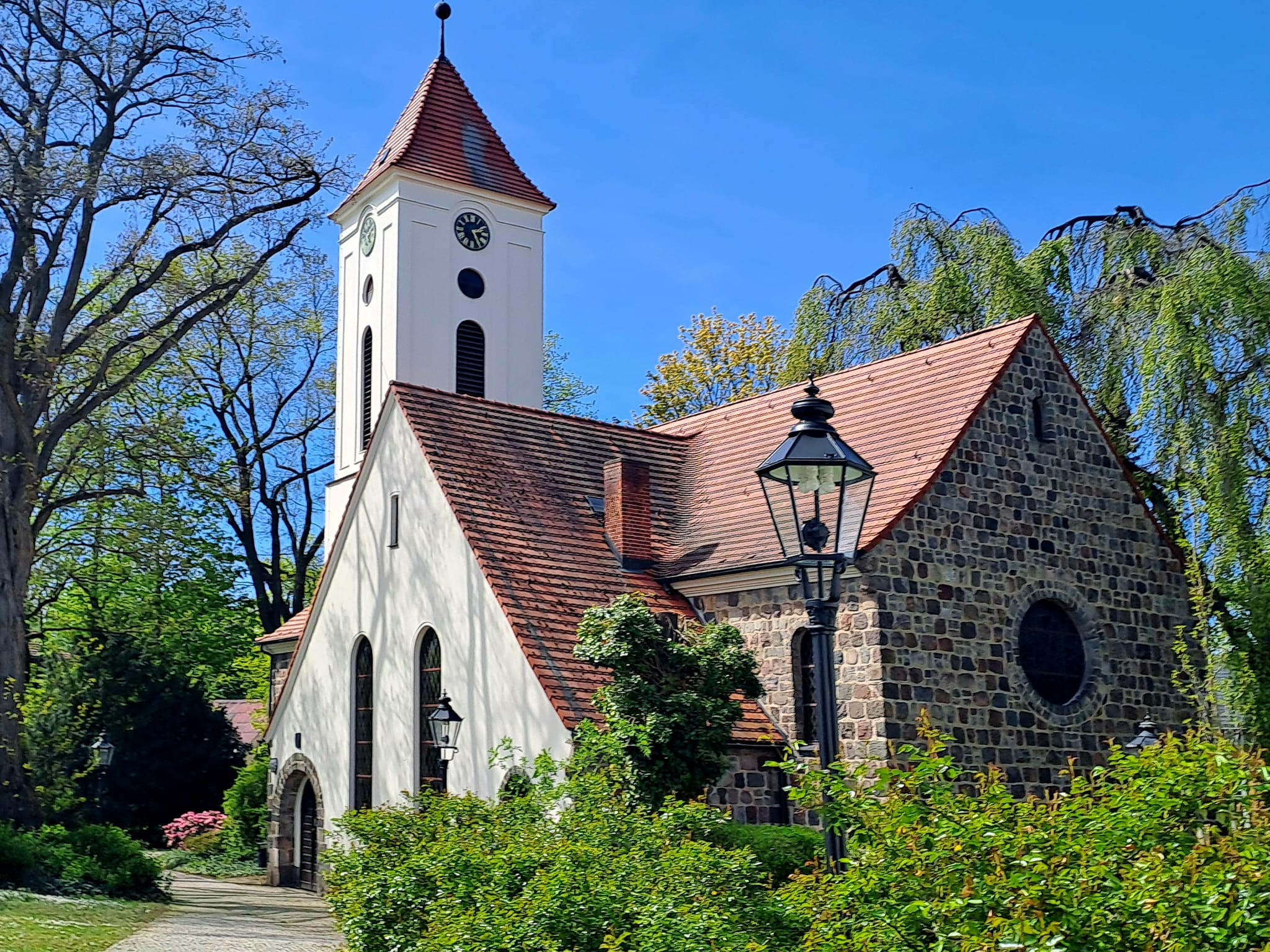 Kirchengebäude mit Turm und rotem Dach zwischen kahlen Bäumen.