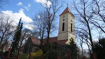 Kirche mit hohem Turm und rotem Dach, umgeben von Bäumen.