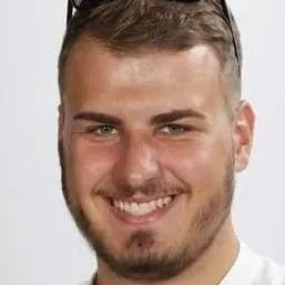 Lächelnder junger Mann mit kurzem Bart und dunklem Haar.