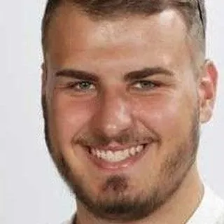 Lächelnder junger Mann mit kurzem Bart und dunklem Haar.