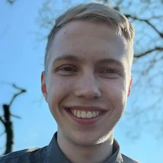Lächelnder junger Mann mit blonden Haaren unter blauem Himmel.