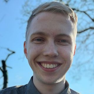 Lächelnder junger Mann mit blonden Haaren unter blauem Himmel.