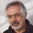 Lächelnder Mann mit grauem Haar, Bart und Brille.