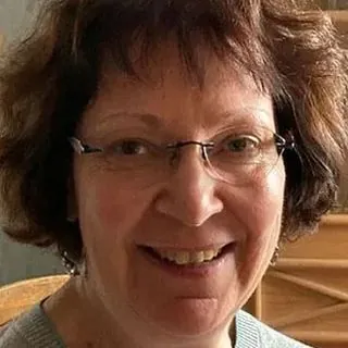 Lächelnde Frau mit kurzen braunen Haaren und Brille.