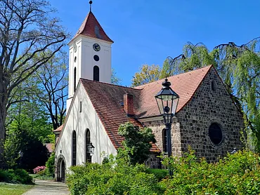 Kirchengebäude mit Turm und rotem Dach zwischen kahlen Bäumen.