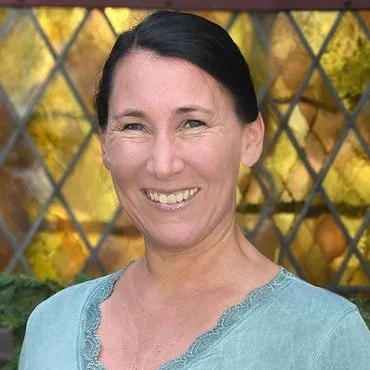 Porträt einer fröhlichen Frau vor einem gemusterten Fenster.