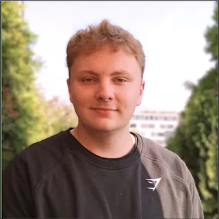 Lächelnde Frau mit dunklen Haaren und Brille, Ziegelstein-Hintergrund.