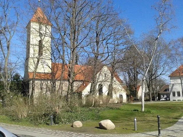 Kirchengebäude mit Turm und rotem Dach zwischen kahlen Bäumen.