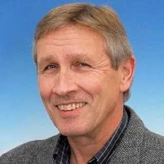 Lächelnder Mann mit kurzen Haaren und Jacke, blauer Hintergrund.