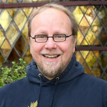 Lächelnder Mann im Kapuzenpulli mit Brille, Buntglas-Hintergrund.