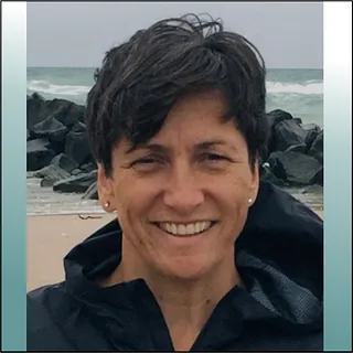 Lächelnde Frau mit kurzen Haaren und Jacke, blauer Hintergrund.