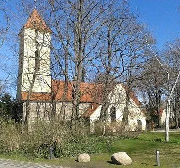 Kirchengebäude mit Turm und rotem Dach zwischen kahlen Bäumen.