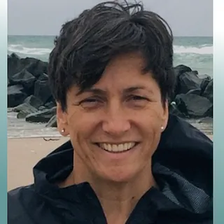 Lächelnde Frau mit kurzen Haaren und Jacke, blauer Hintergrund.