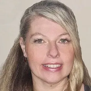 Lächelnde Frau mit langen grau-blonden Haaren und Ohrringen.