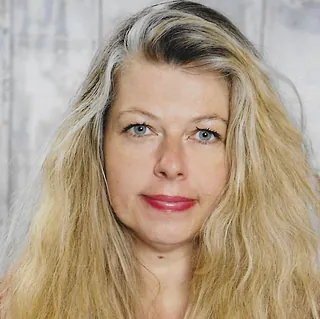 Lächelnde Frau mit langen grau-blonden Haaren und Ohrringen.